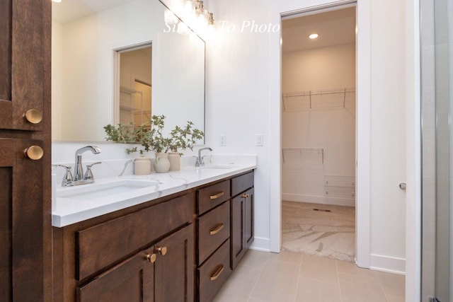 full bathroom with double vanity, a sink, a walk in closet, and tile patterned floors