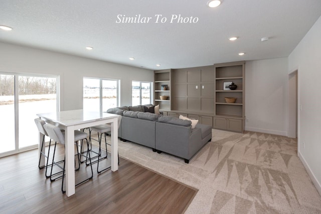 living area featuring a textured ceiling, recessed lighting, light wood-style flooring, and baseboards