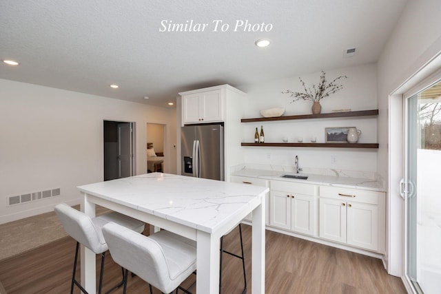 kitchen featuring white cabinets, stainless steel fridge, visible vents, and open shelves