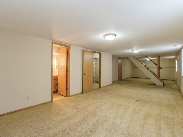 finished below grade area featuring stairs, baseboards, and light colored carpet