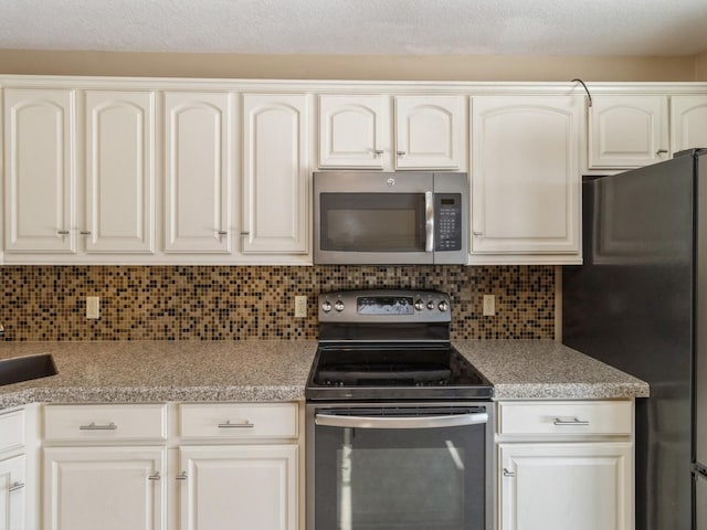 kitchen featuring range with electric stovetop, white cabinets, backsplash, freestanding refrigerator, and stainless steel microwave