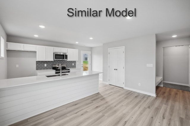 kitchen featuring light countertops, stainless steel microwave, backsplash, white cabinets, and a sink