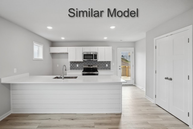 kitchen with white cabinets, a peninsula, stainless steel appliances, light countertops, and a sink