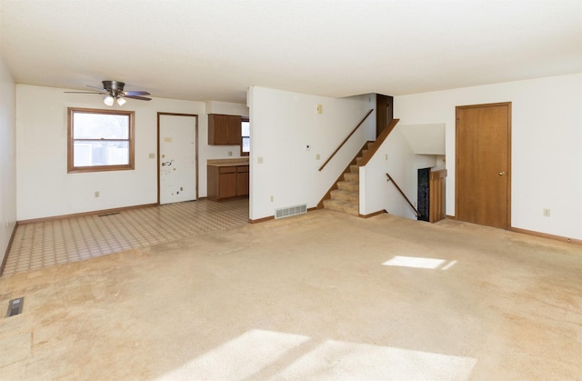 unfurnished living room with visible vents, light colored carpet, stairway, and baseboards