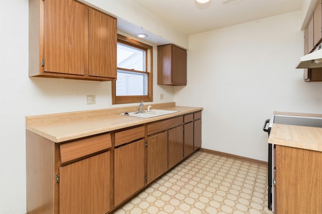 kitchen featuring light floors, light countertops, a sink, range with electric cooktop, and baseboards