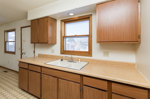 kitchen with light floors, light countertops, brown cabinetry, a sink, and baseboards