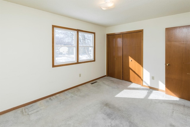 unfurnished bedroom with a closet, visible vents, light carpet, and baseboards