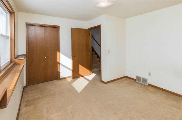 unfurnished bedroom with light carpet, a closet, visible vents, and baseboards