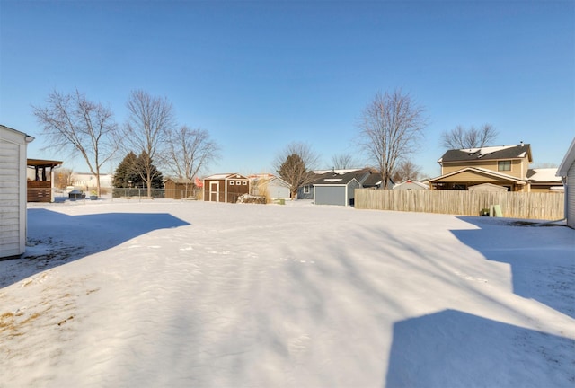 snowy yard with a residential view, an outdoor structure, fence, and a shed