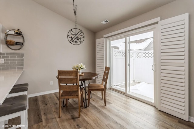 dining space featuring light wood-style floors, lofted ceiling, visible vents, and baseboards