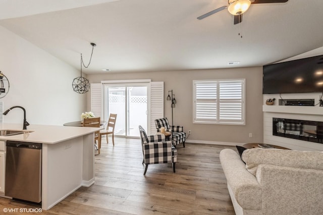 living room featuring lofted ceiling, light wood-style flooring, a ceiling fan, baseboards, and a glass covered fireplace