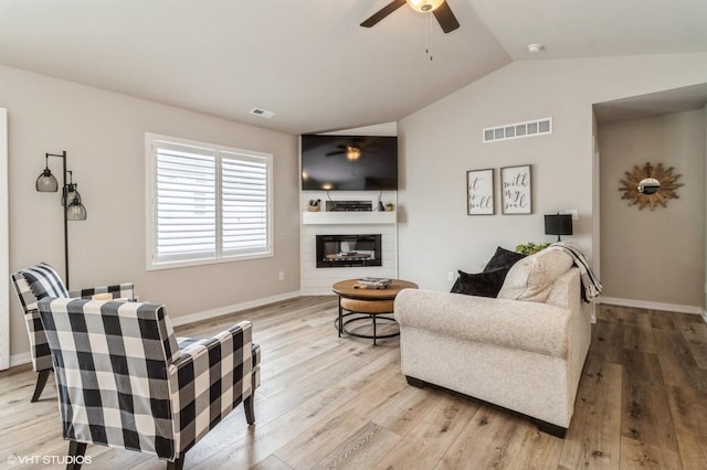 living area featuring visible vents, a ceiling fan, a glass covered fireplace, lofted ceiling, and light wood-style floors