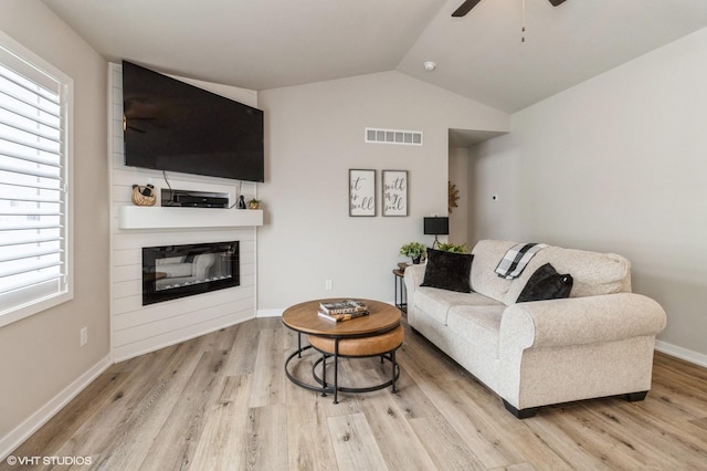 living room featuring a glass covered fireplace, visible vents, vaulted ceiling, and light wood finished floors