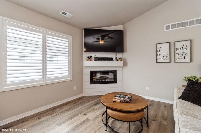 living area featuring visible vents, wood finished floors, and a glass covered fireplace