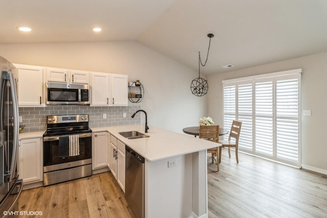 kitchen featuring stainless steel appliances, a peninsula, a sink, hanging light fixtures, and light countertops