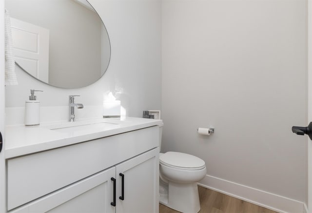 half bath with toilet, baseboards, wood finished floors, and vanity