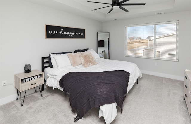 bedroom with light carpet, a tray ceiling, visible vents, and baseboards