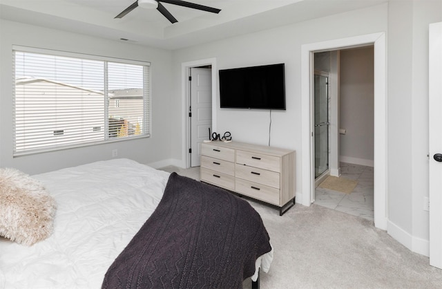 bedroom with a raised ceiling, light colored carpet, ensuite bathroom, ceiling fan, and baseboards