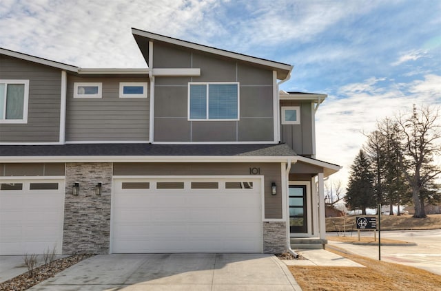 multi unit property featuring a garage, stone siding, board and batten siding, and driveway