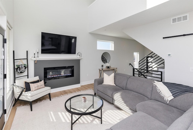 living room featuring visible vents, baseboards, stairs, light wood-type flooring, and a glass covered fireplace