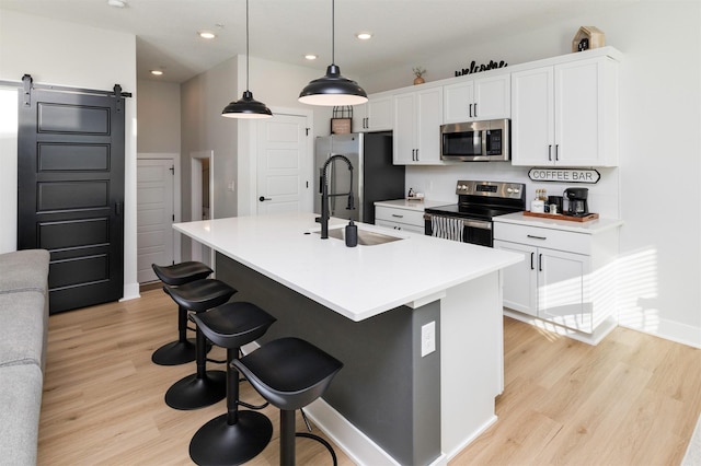 kitchen featuring a barn door, decorative light fixtures, stainless steel appliances, light countertops, and a center island with sink