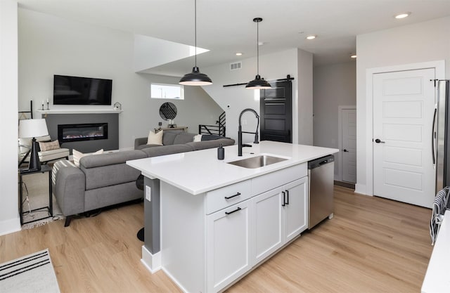 kitchen with decorative light fixtures, light countertops, white cabinets, a kitchen island with sink, and dishwasher