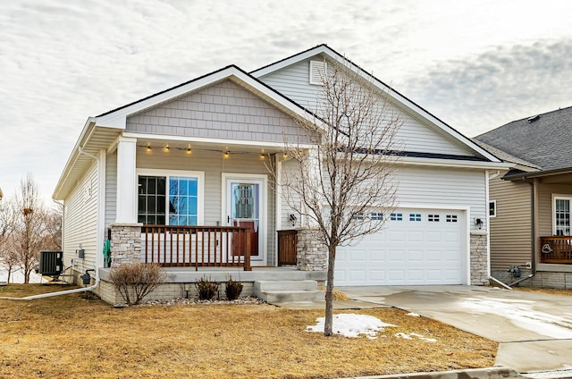 view of front of home featuring driveway, a garage, central AC unit, stone siding, and a porch