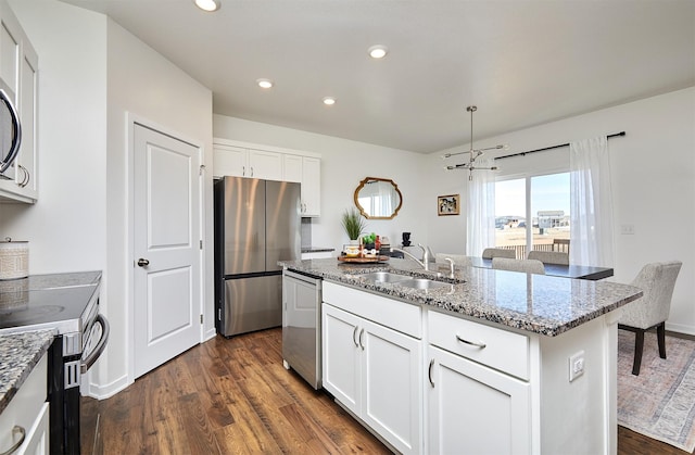 kitchen with light stone counters, a kitchen island with sink, a sink, white cabinetry, and appliances with stainless steel finishes