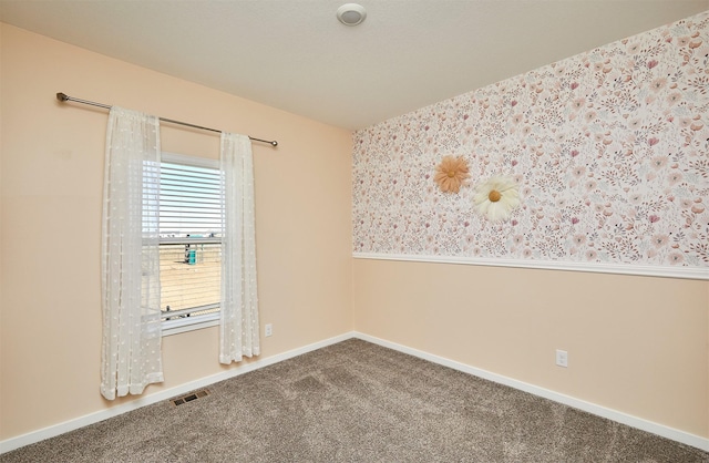 carpeted empty room with a wainscoted wall, visible vents, baseboards, and wallpapered walls