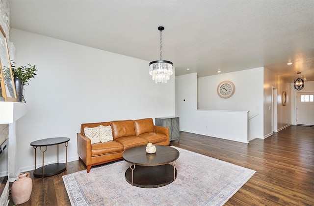 living area featuring dark wood-style floors, a fireplace, baseboards, and a notable chandelier