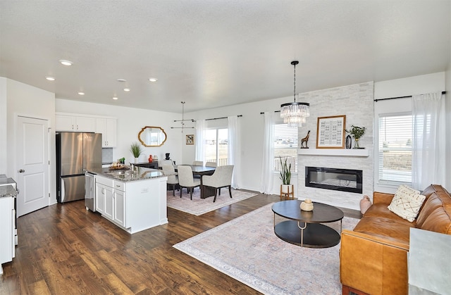 living area with a chandelier, a wealth of natural light, dark wood-style flooring, and a fireplace