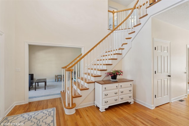 stairway with a towering ceiling, visible vents, baseboards, and wood finished floors