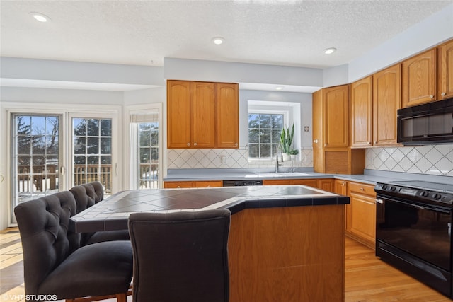 kitchen with a sink, light wood-type flooring, tile counters, decorative backsplash, and black appliances