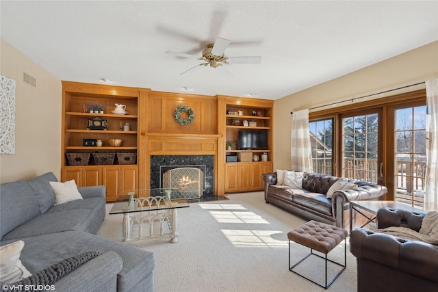 living area featuring built in shelves, visible vents, a premium fireplace, a ceiling fan, and light carpet