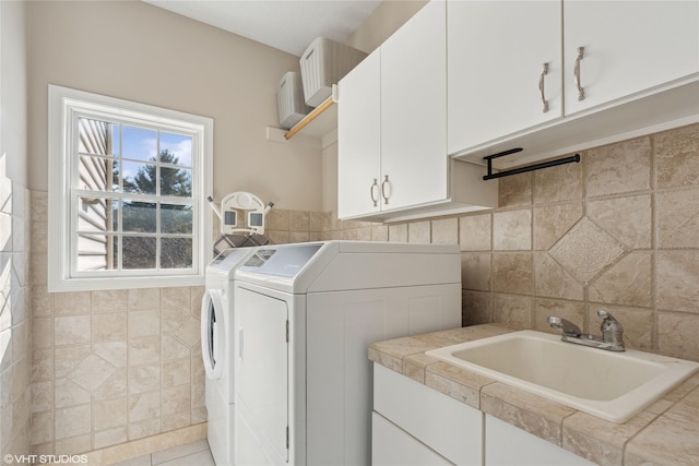 washroom with washer and clothes dryer, a sink, cabinet space, and tile walls