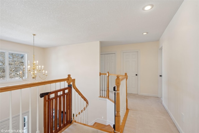 hall with a textured ceiling, light colored carpet, an upstairs landing, baseboards, and an inviting chandelier