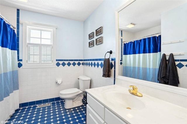 bathroom with visible vents, wainscoting, toilet, vanity, and tile walls