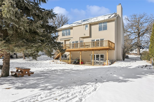 snow covered house with a chimney and a wooden deck