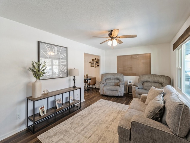 living room featuring a textured ceiling, ceiling fan, dark wood-style flooring, and baseboards