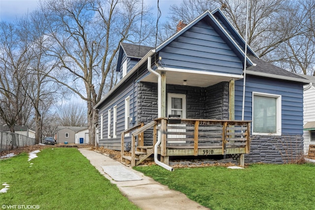 bungalow-style home featuring a deck, stone siding, a shingled roof, and a front yard