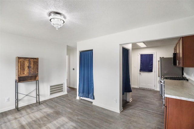 interior space featuring dark wood-style flooring, a notable chandelier, visible vents, a textured ceiling, and baseboards