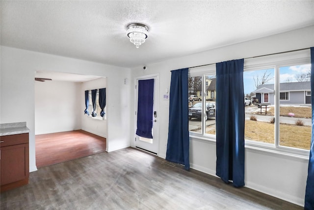 empty room featuring a textured ceiling, baseboards, wood finished floors, and an inviting chandelier