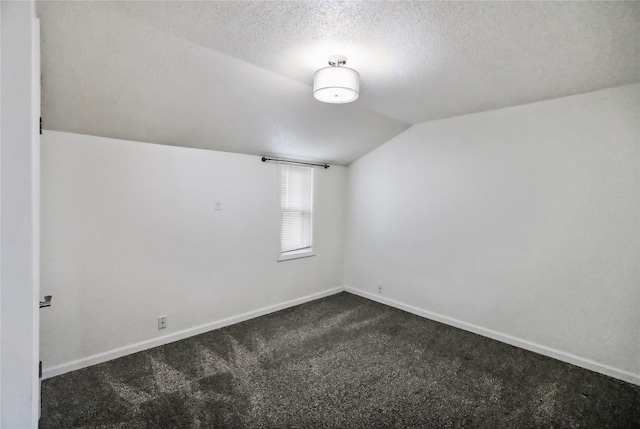 spare room featuring lofted ceiling, dark carpet, a textured ceiling, and baseboards