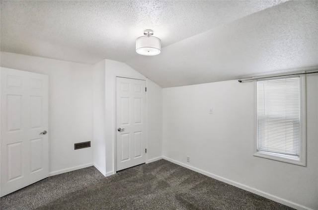 bonus room featuring a textured ceiling, dark carpet, lofted ceiling, and baseboards