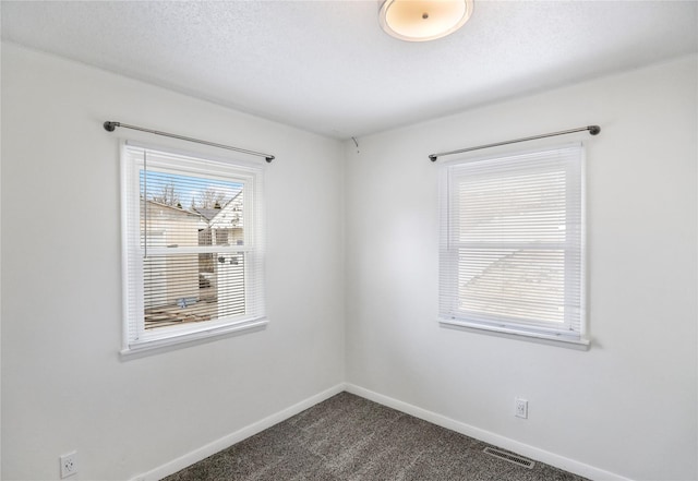 empty room featuring a textured ceiling, dark colored carpet, visible vents, and baseboards