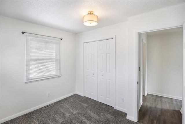 unfurnished bedroom with baseboards, visible vents, dark colored carpet, a textured ceiling, and a closet