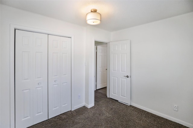 unfurnished bedroom featuring baseboards, dark carpet, and a closet