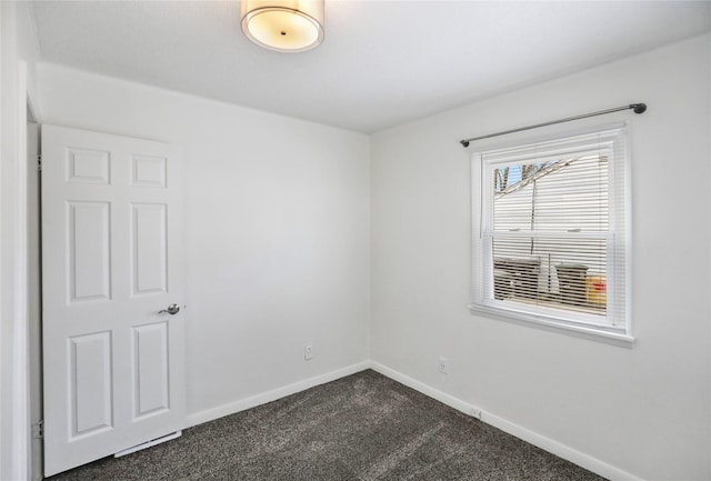 spare room with dark colored carpet and baseboards