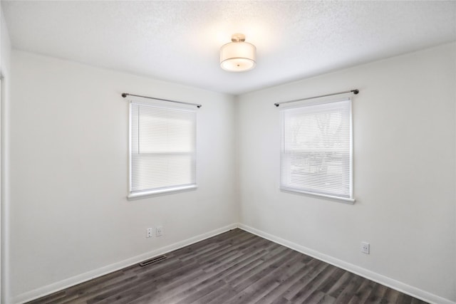 spare room with a textured ceiling, dark wood-style flooring, visible vents, and baseboards