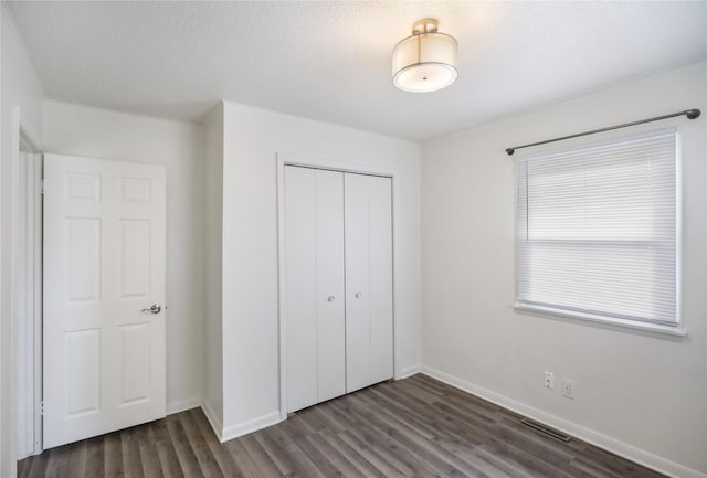 unfurnished bedroom with dark wood-type flooring, a closet, visible vents, and baseboards